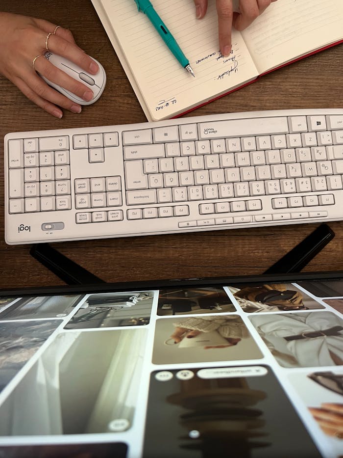 Overhead view of a workspace with keyboard, mouse, and a person planning in a notebook.