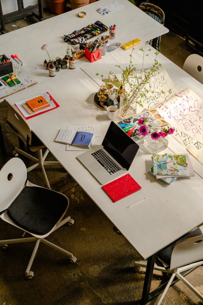 Bright overhead view of a creative workspace with a laptop, notebooks, and art supplies.